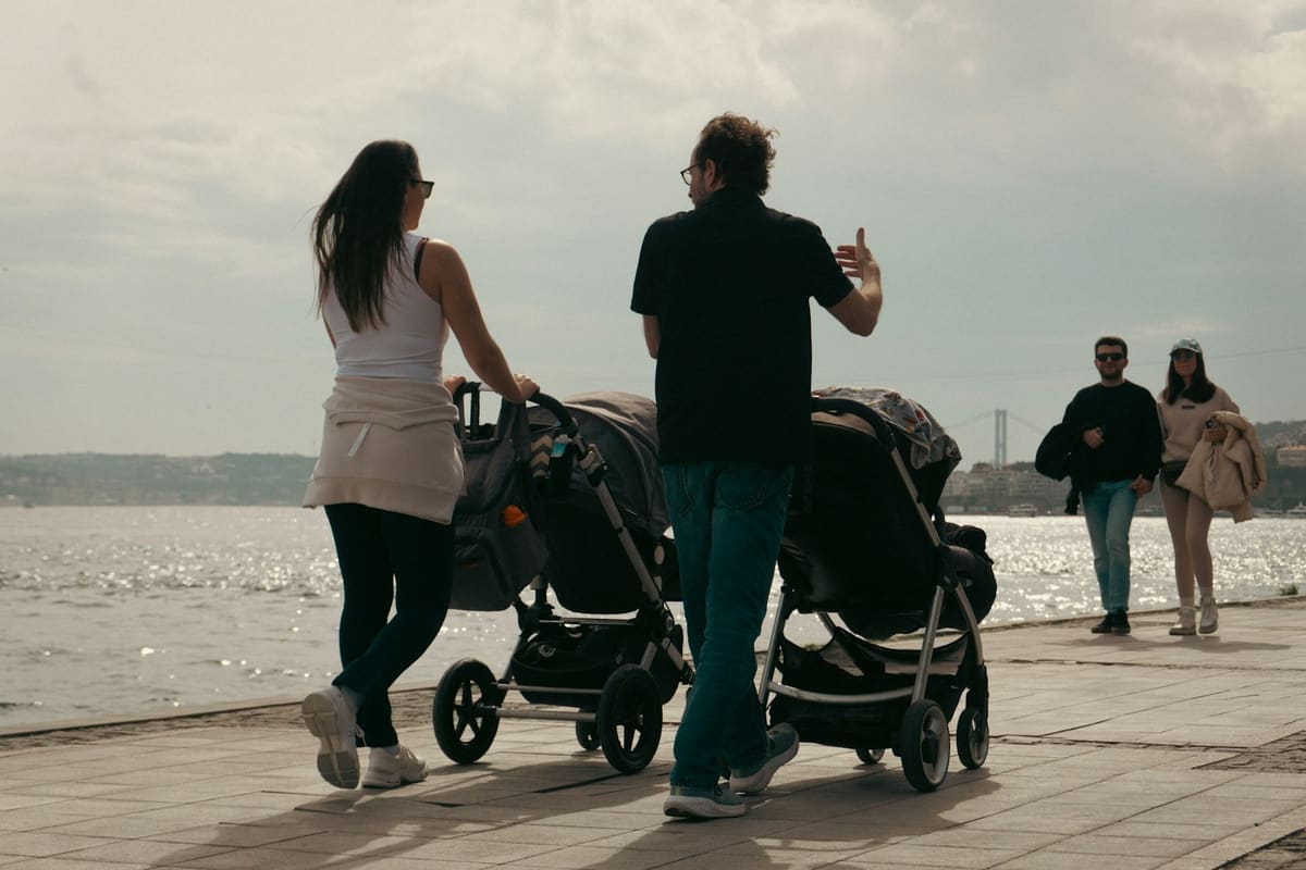 Eine Frau und ein Mann gehen mit Kinderwagen am Wasser spazieren und unterhalten sich