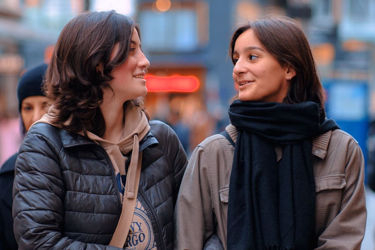 Zwei junge Frauen schlendern durch eine Stadtstrasse und unterhalten sich freundlich